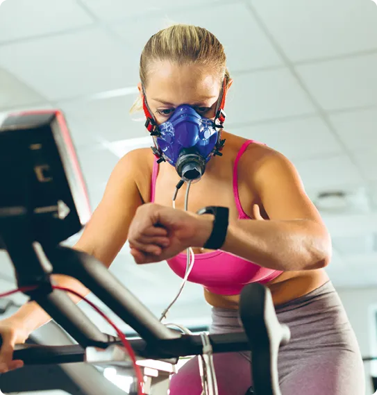 Femme s'entraînant avec un masque à oxygène sur un vélo d'appartement.