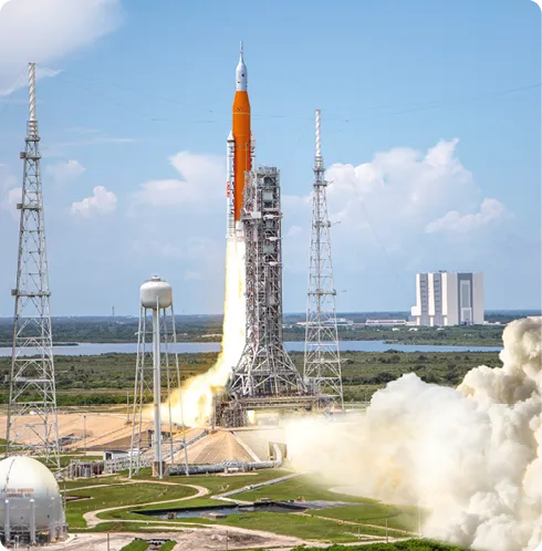 Lancement d'une fusée, flamme et fumée à la base, sur fond de ciel bleu.