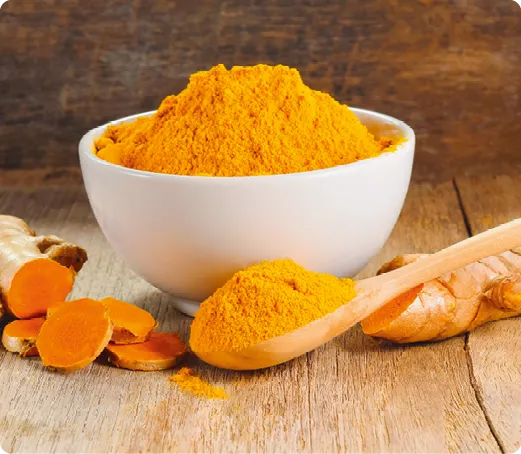 Poudre de curcuma orange vif dans un bol blanc, racine et cuillère en bois sur table.