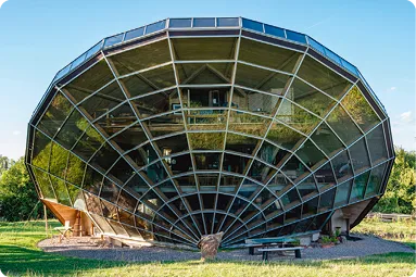 Bâtiment sphérique vitré sur herbe, structure futuriste, ciel bleu.