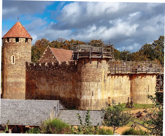 Photographie du château médiéval de Guédelon en construction.  Murs de pierre, tours et échafaudages visibles.