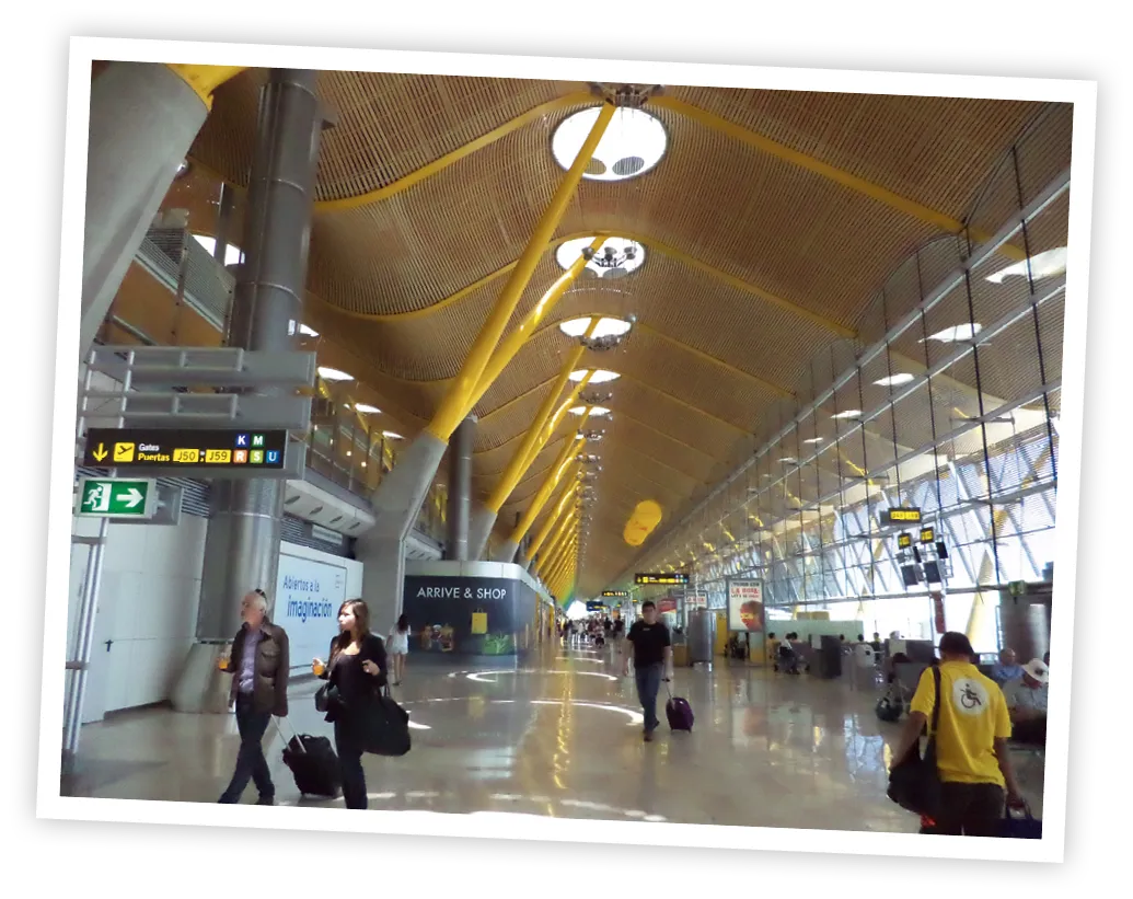 Intérieur de la Terminal 4 de l'aéroport de Madrid-Barajas avec des passagers et des panneaux de signalisation sous un plafond ondulé en bambou.