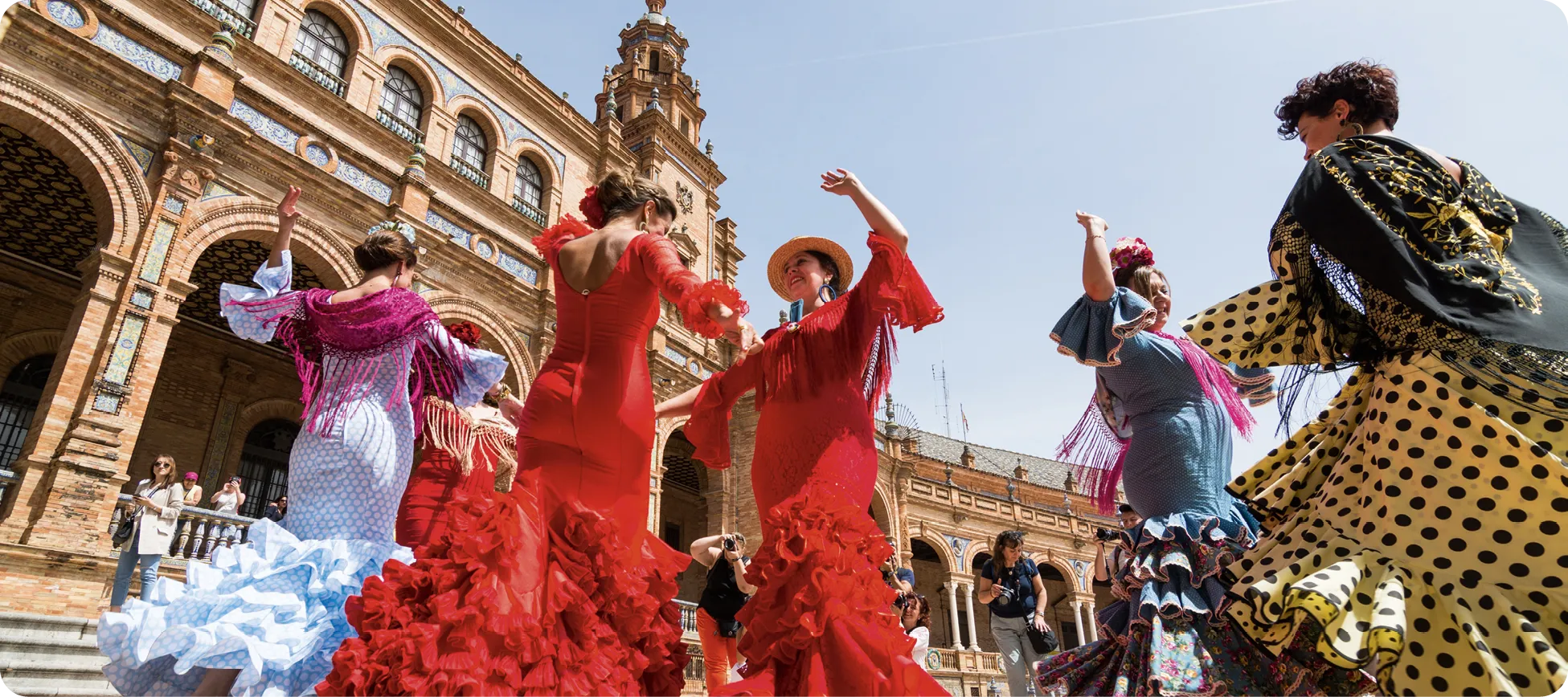 Mujeres vestidas de flamenca bailando sevillanas en la Plaza de España de Sevilla.