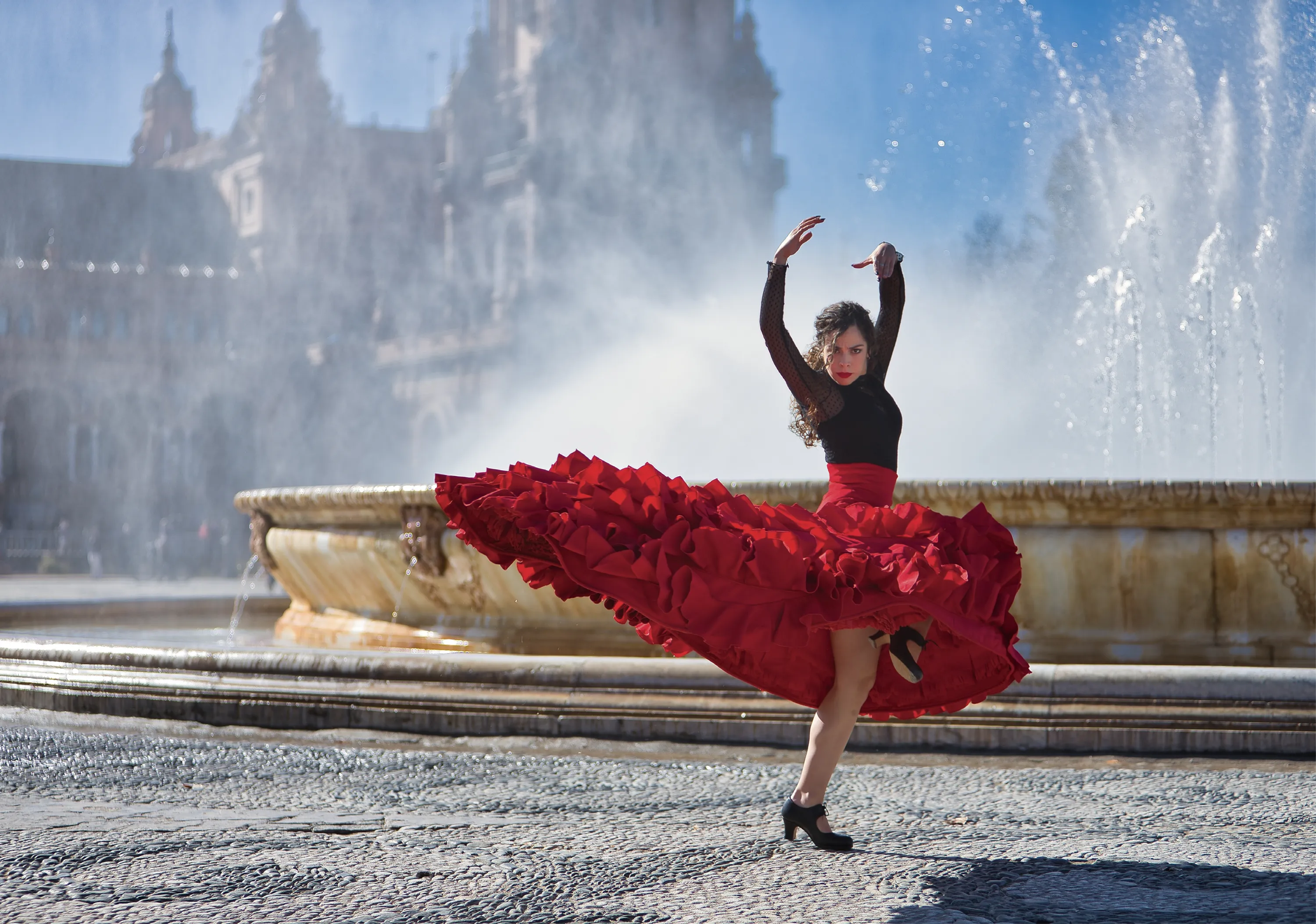 Une danseuse de flamenco vêtue d'une robe rouge et d'un haut noir danse devant une fontaine monumentale.