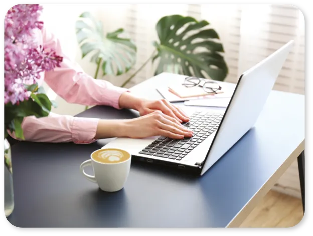 A person typing on a laptop with a cup of coffee and flowers.