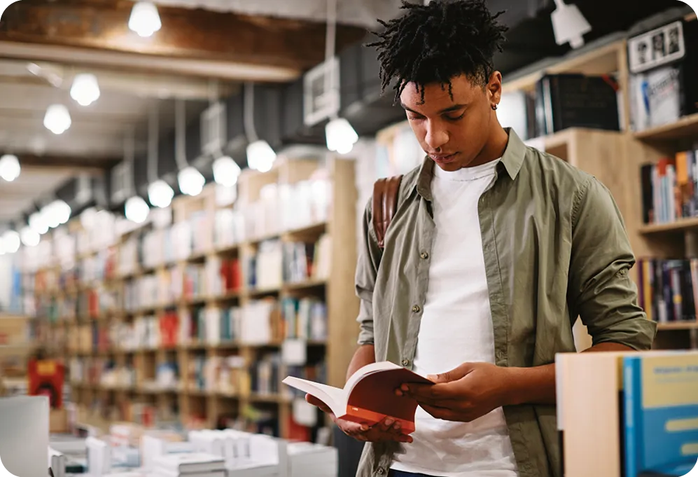 Un étudiant afro-américain lisant un livre en se tenant à la librairie.