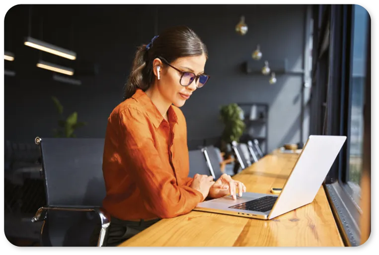 Young business woman working on laptop computer at office desk with city view.