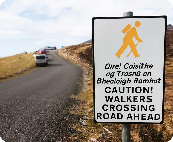 Signez en irlandais et en anglais, avertissant les automobilistes que les marcheurs traversent la route en avant.
