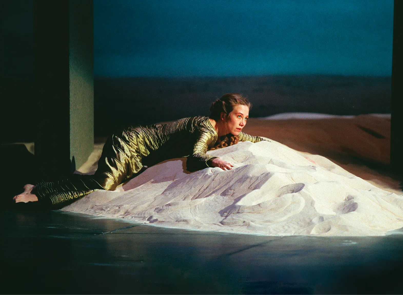 Photographie de scène : Valérie Dréville, dans le rôle de Phèdre, allongée sur un monticule de sable. Mise en scène de Luc Bondy (Odéon-Théâtre de l'Europe, 1998).