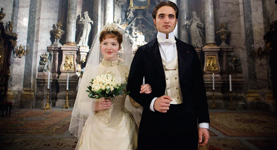 Capture du film Bel Ami (2012) : Robert Pattinson et Holliday Grainger, mariés, se tiennent par le bras dans une église.