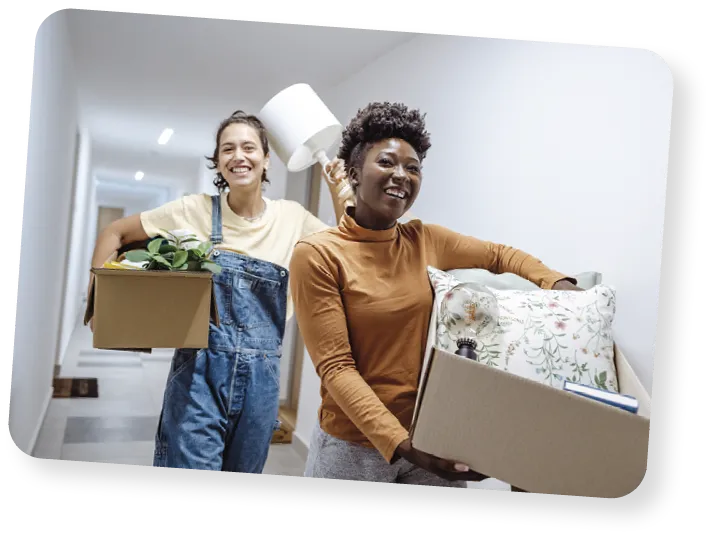 Two female friends carrying cardboard boxes with belongings and moving into campus