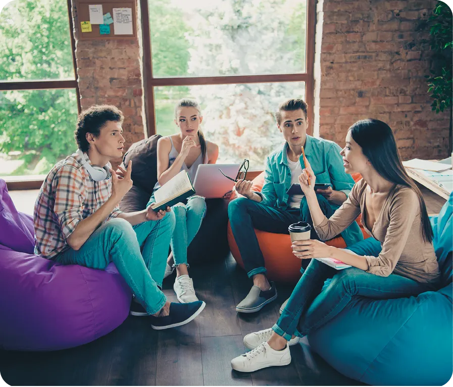 Quatre étudiants discutent assis sur des poufs colorés dans un espace de travail décontracté.