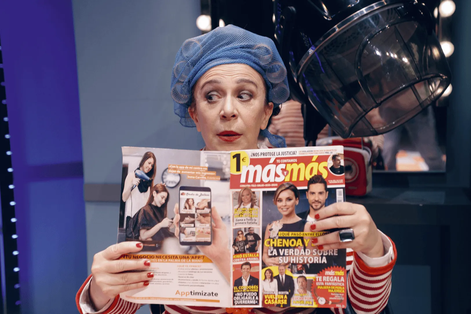 Photographie d'une femme lisant un magazine dans un salon de coiffure. Elle porte un bonnet de bain bleu. L'image provient de la série télévisée humoristique &quotPels pèls" (2017).