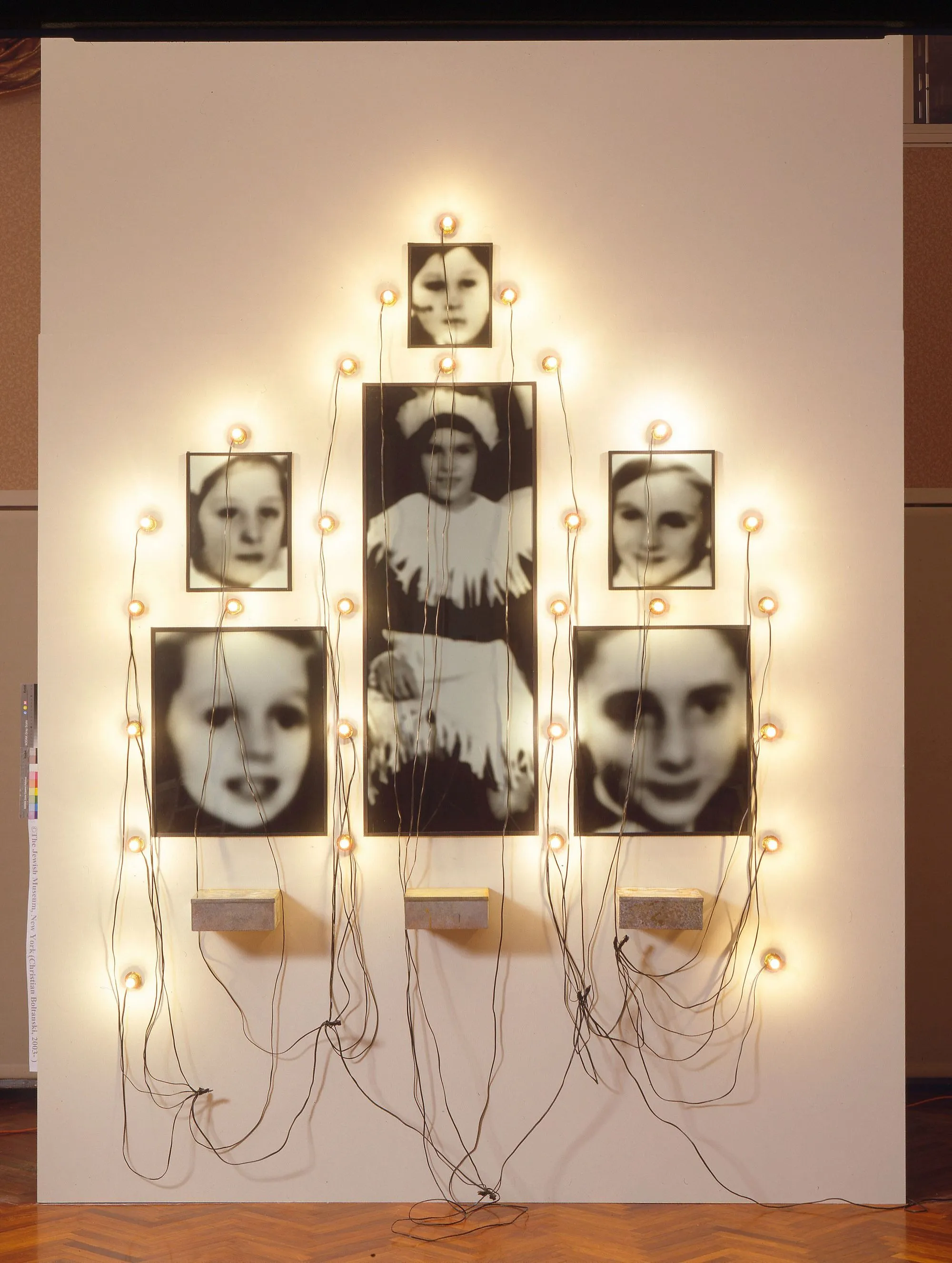 Christian Boltanski, Monument Odessa, 1989, installation : photographies noir et blanc et trois boîtes à biscuits, lampes et fils, 203,2 × 182,9 cm, Marian Goodman Gallery, New York.