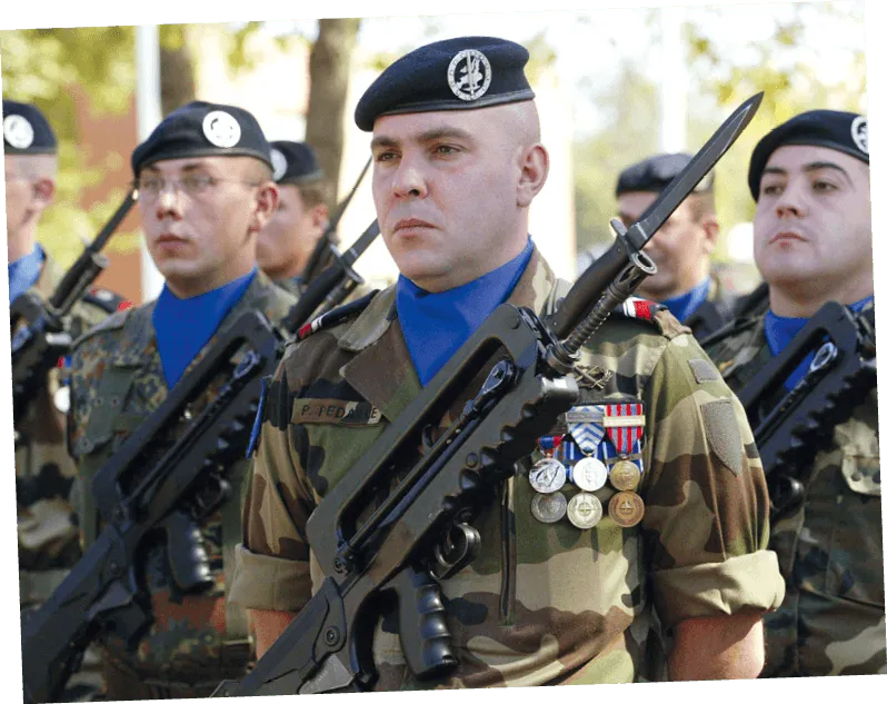 Photographie de soldats français en uniforme, tenant des fusils, lors d'une parade militaire. Détail des décorations sur l'uniforme.