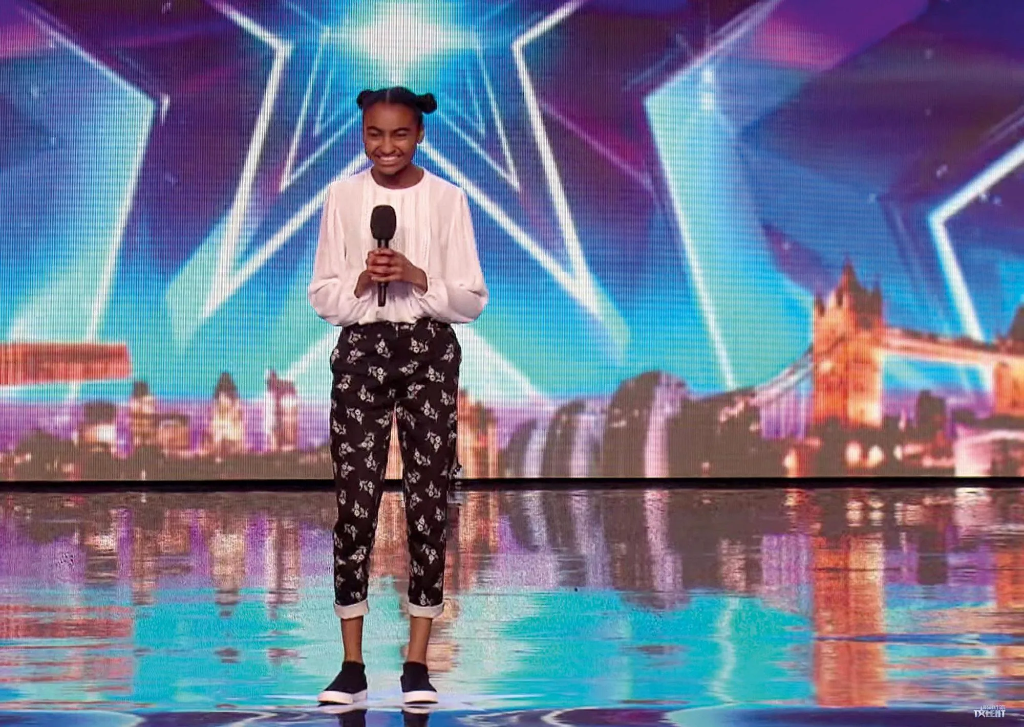 Image de l'émission Britain's Got Talent. Une jeune fille se tient debout sur une scène avec un micro à la main.