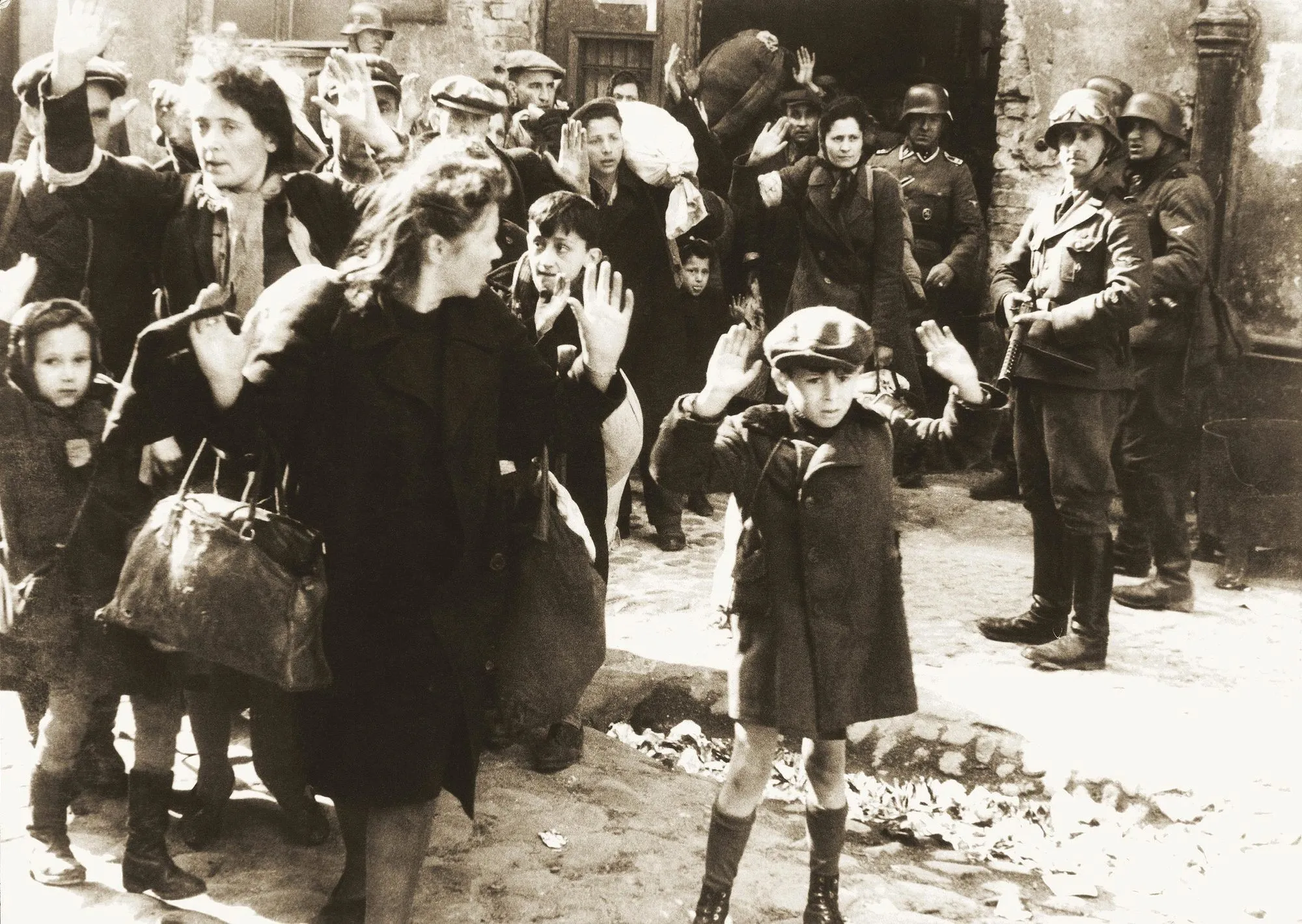 Photographie : civils juifs, dont des enfants, arrêtés par des soldats nazis lors de l'insurrection du ghetto de Varsovie.  Mains levées, regards apeurés.