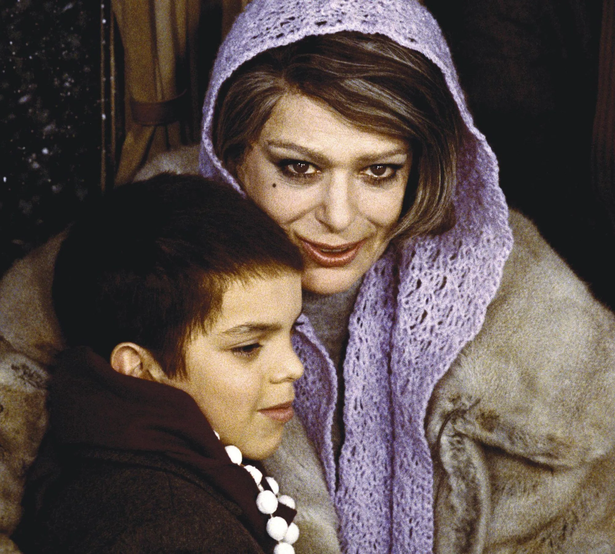 Photographie d'une femme et d'un enfant. La femme porte un châle violet et une fourrure. L'enfant est blotti contre elle. Scène tendre et intime.