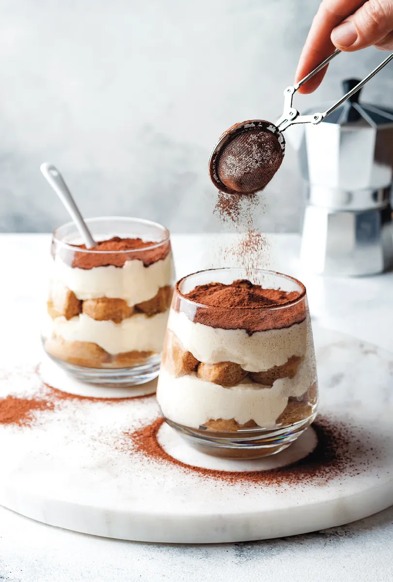 photo de tiramisu en verrine en train d'être saupoudré de cacao