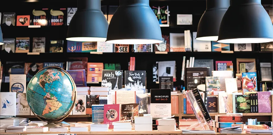 Photo de l'intérieur d'une librairie, des étagères et tables sont remplies de livres.