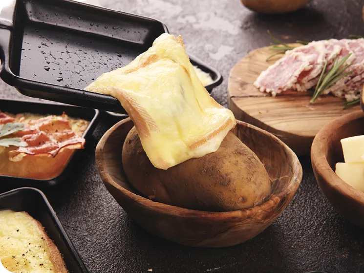 photo d'une délicieuse raclette traditionnelle suisse fondue sur une pomme de terre cuite ou cuite en dés, servie dans des pastilles individuelles avec du salami et des pommes de terre