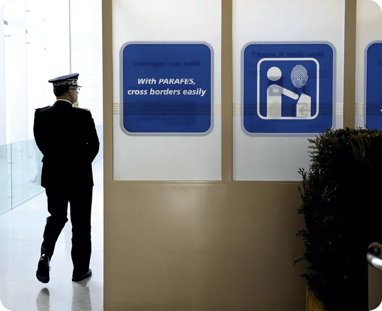 Photographie d'un agent de sécurité marchant dans un aéroport, devant des panneaux indiquant le système PARAFE pour franchir les frontières facilement.