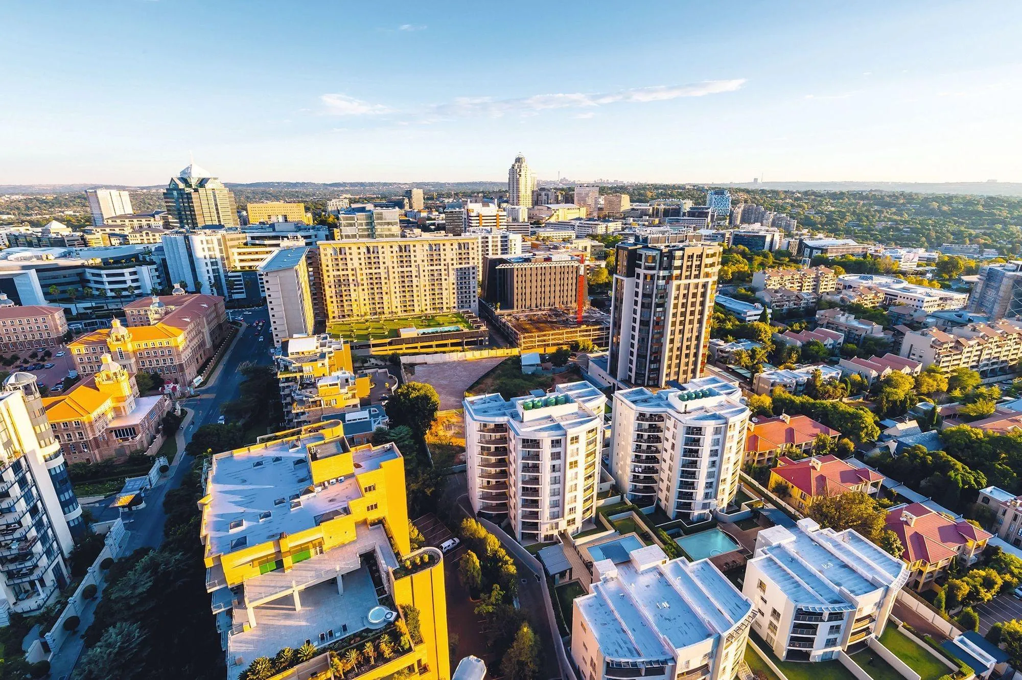 Photographie aérienne de Sandton, en Afrique du Sud, montrant des immeubles résidentiels et de bureaux modernes, ainsi qu'une végétation luxuriante.