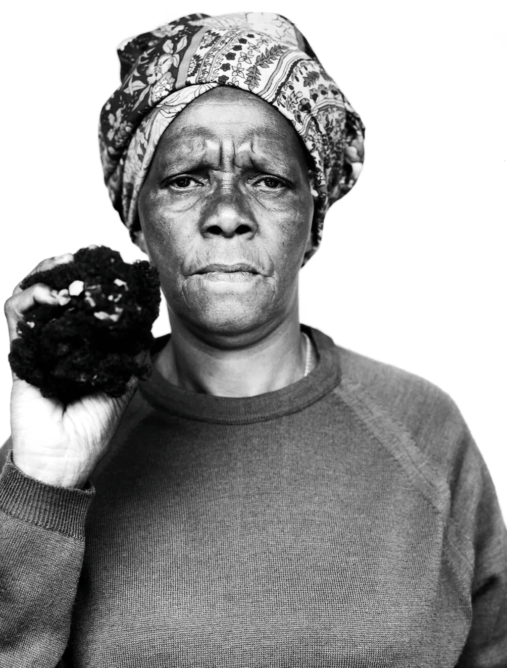 Photographie noir et blanc de Joyce Mtimkulu, femme sud-africaine portant un foulard coloré, tenant un objet sombre.