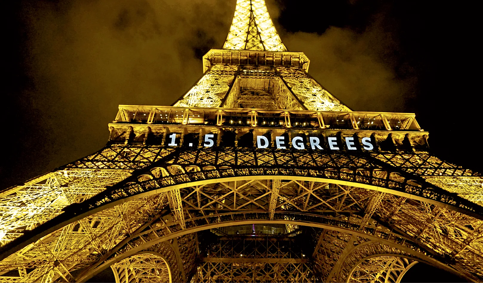 Photographie nocturne de la Tour Eiffel illuminée, affichant &quot1.5 DEGREES" sur sa structure. Gros plan sur les détails architecturaux.