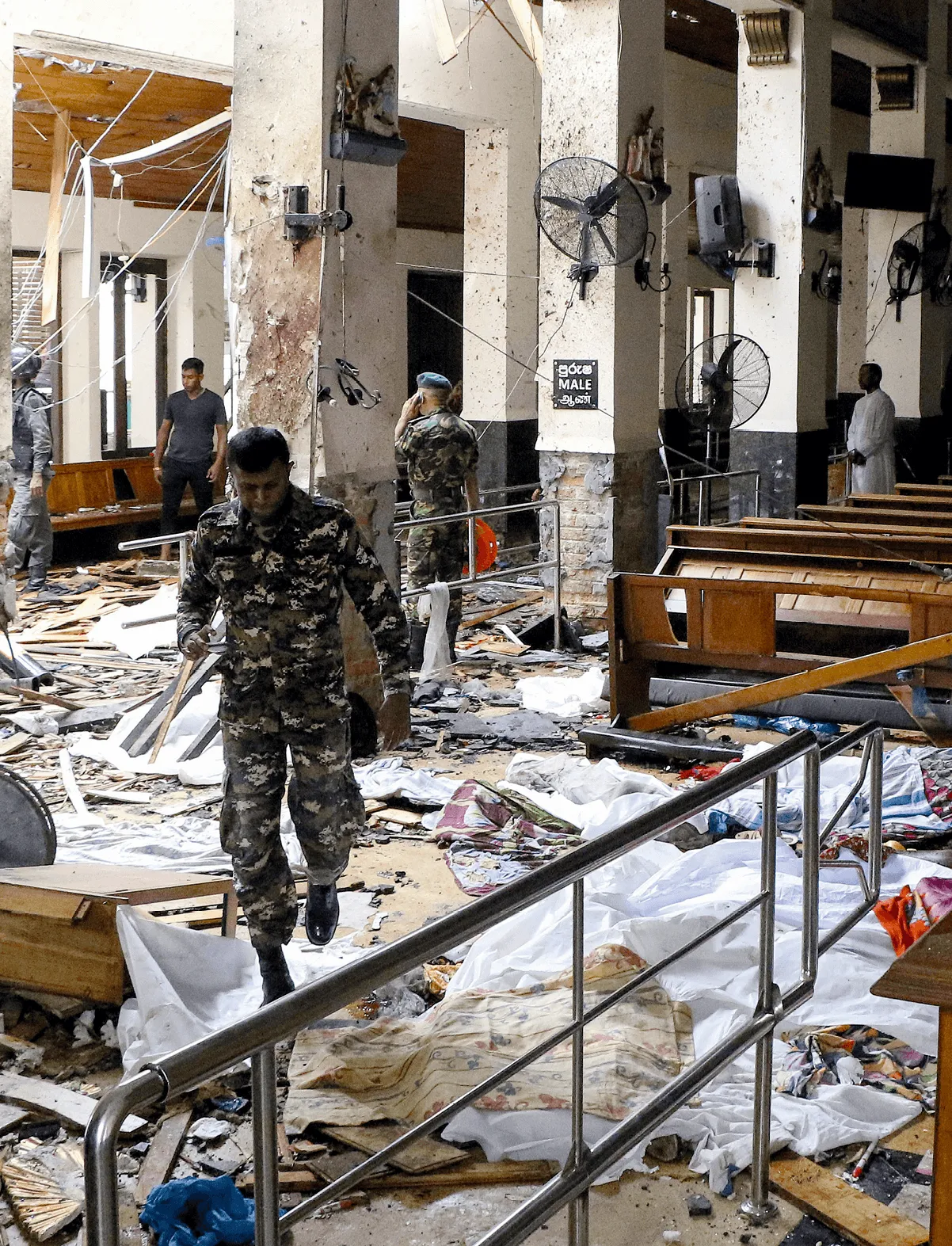 Photographie des attentats de Pâques 2019 au Sri Lanka. Une église détruite, des soldats, des débris et des corps recouverts de draps blancs.