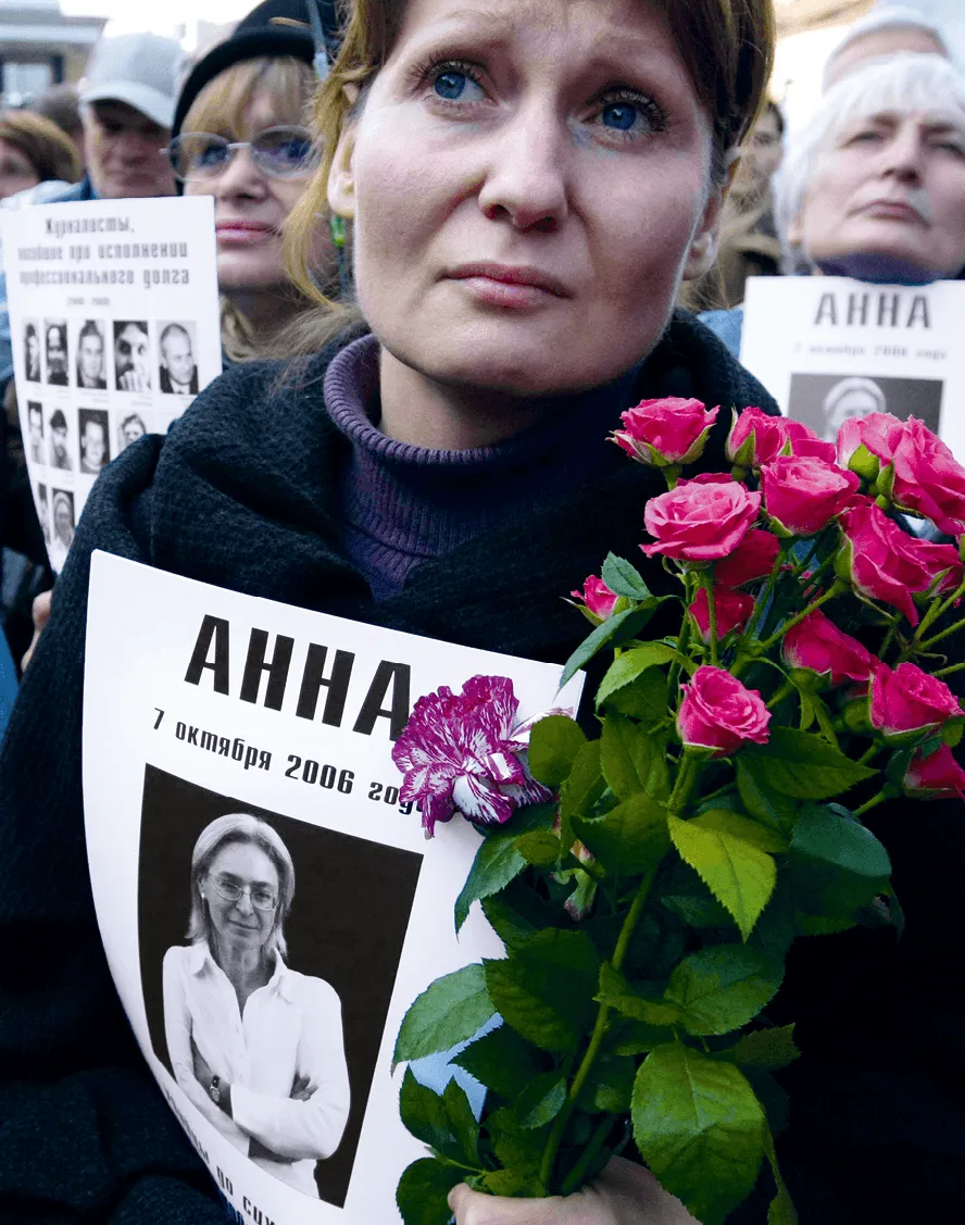 Photographie de 2009 d'Anna Shevelyova à une manifestation en Russie.  Une femme tient un bouquet de roses et une pancarte commémorant Anna Politkovskaïa, journaliste assassinée.