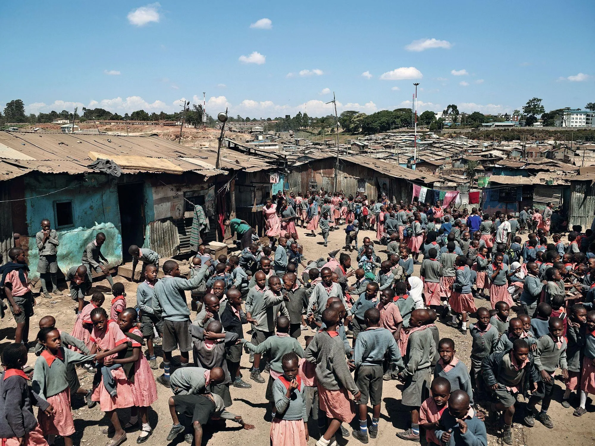 Photographie d'enfants africains jouant dans un bidonville. Ils portent des uniformes scolaires et semblent joyeux malgré leur environnement pauvre.