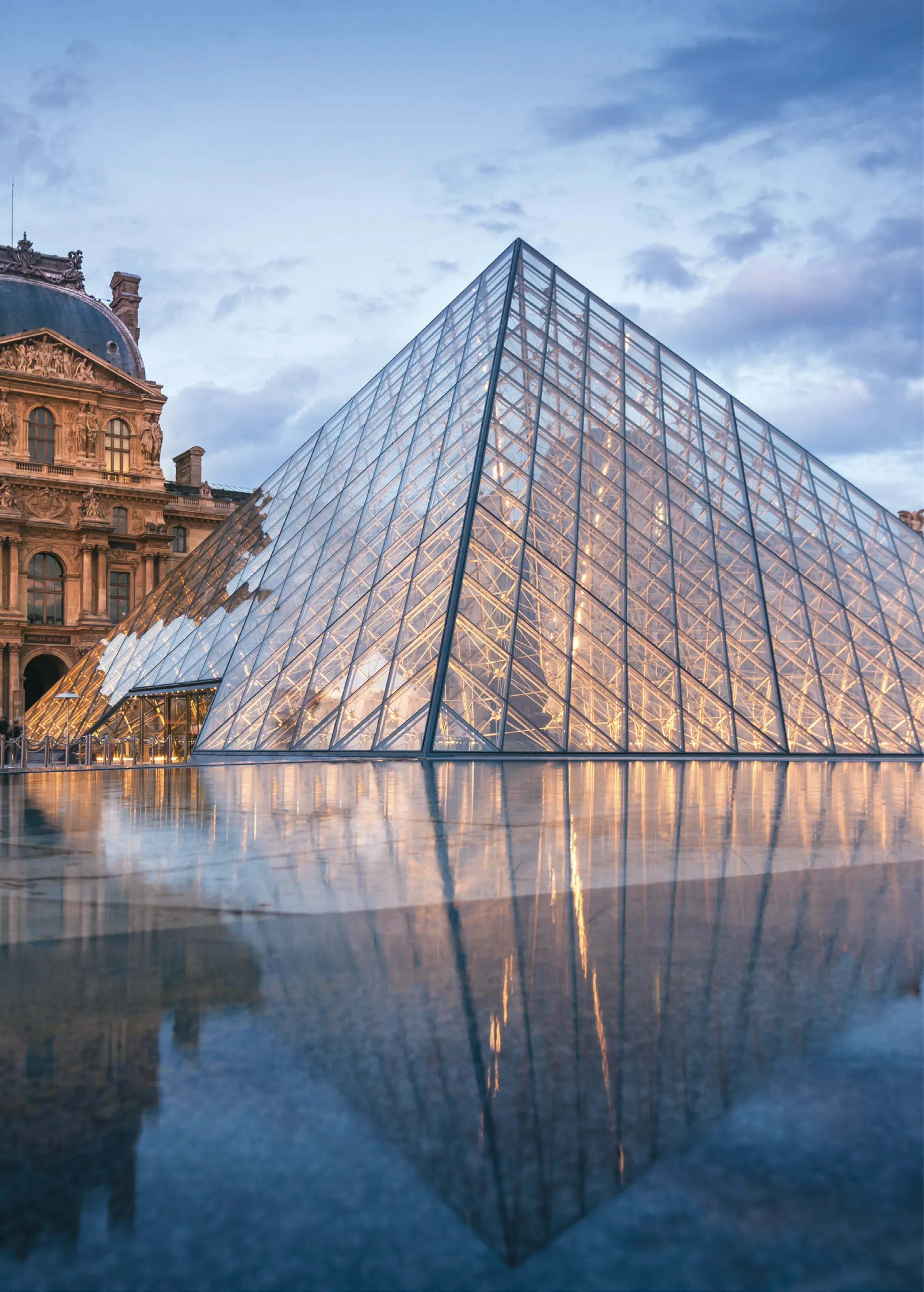 Photo de la pyramide du Louvre éclairée qui se reflète dans le sol mouillée en soirée