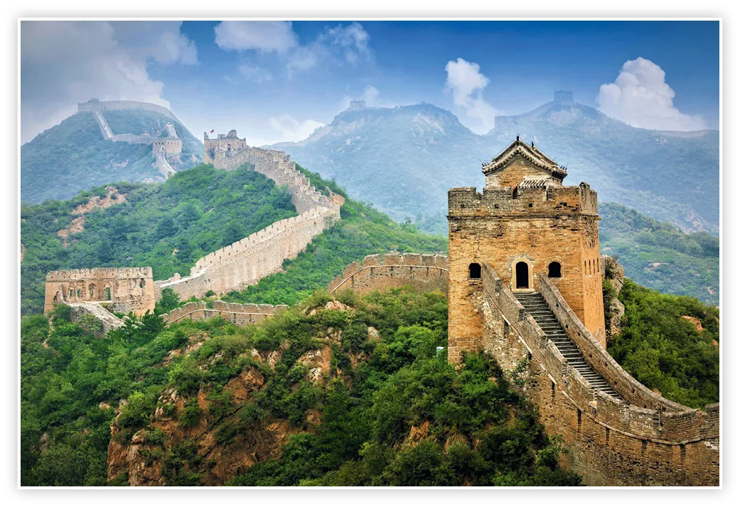 Photographie de la Grande Muraille de Chine serpentant sur des montagnes verdoyantes. Une tour de guet imposante est au premier plan.