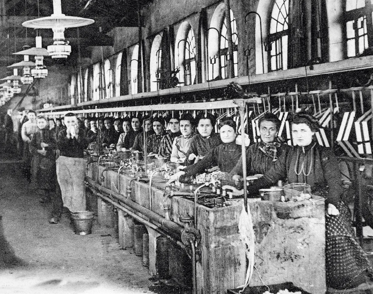 Photographie d'ouvrières dans une filature de soie vers 1900. Elles travaillent sur de longues machines, concentrées sur leur tâche. Ambiance industrielle du début du XXe siècle.