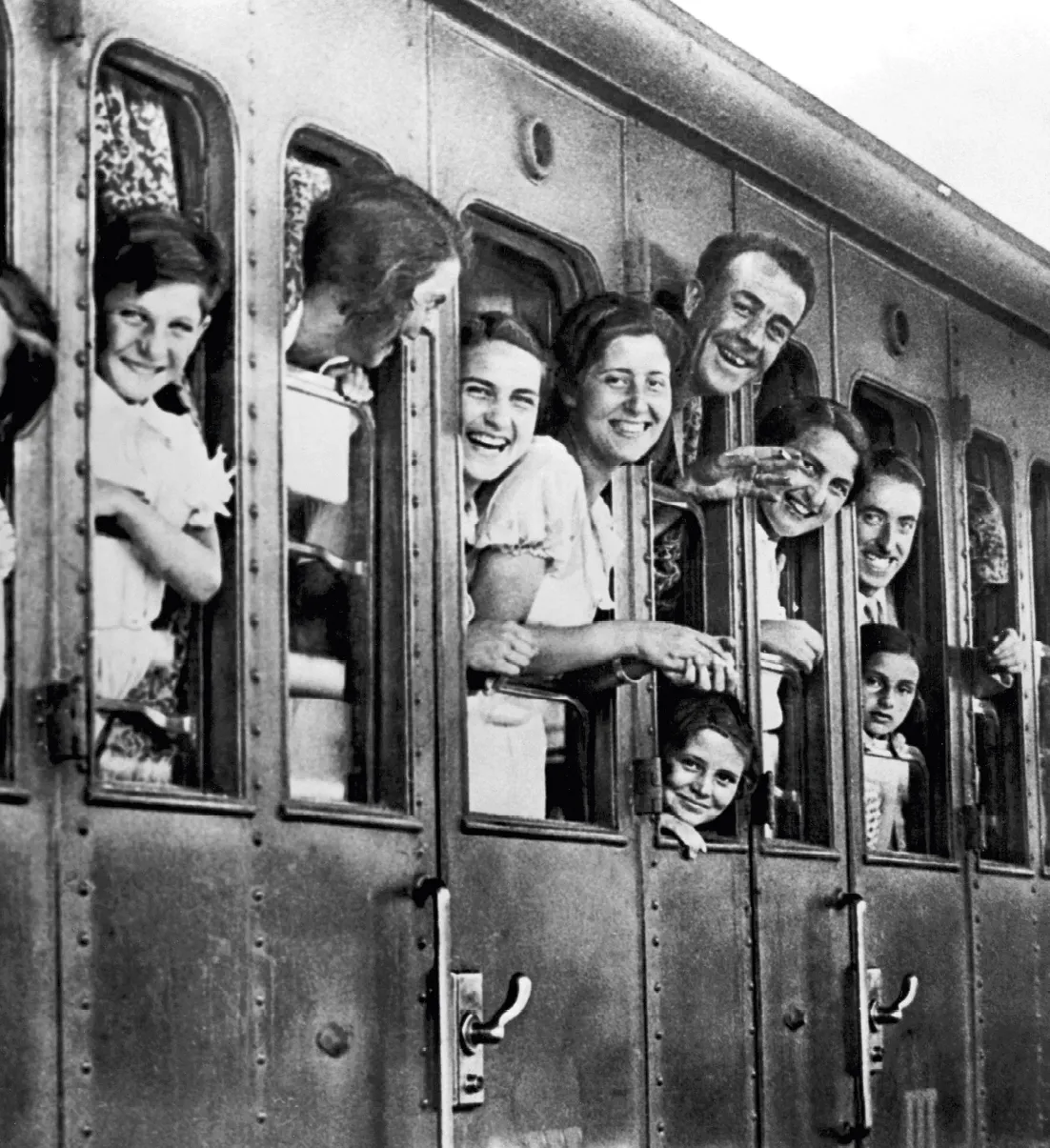 Photographie en noir et blanc : groupe souriant de passagers dans un train, regardant par les fenêtres.