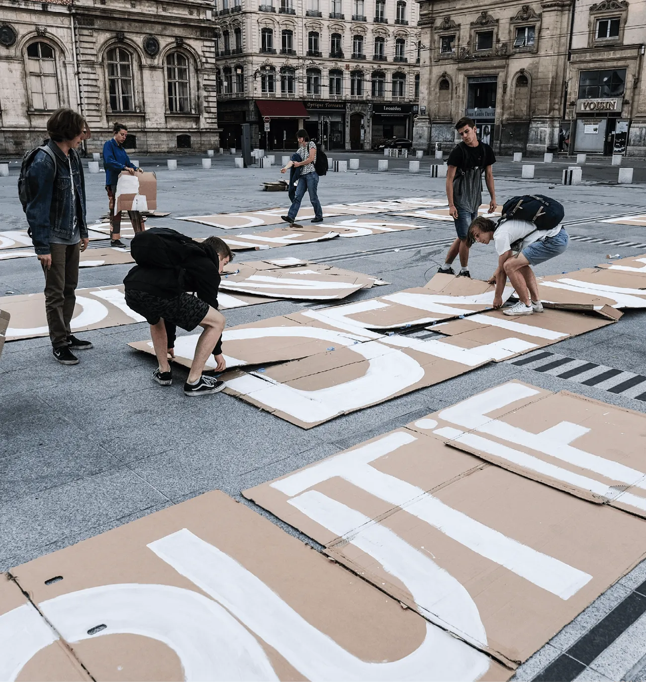 Photographie de jeunes activistes de Youth For Climate préparant une manifestation. Ils peignent des slogans sur des cartons disposés au sol d'une place publique.