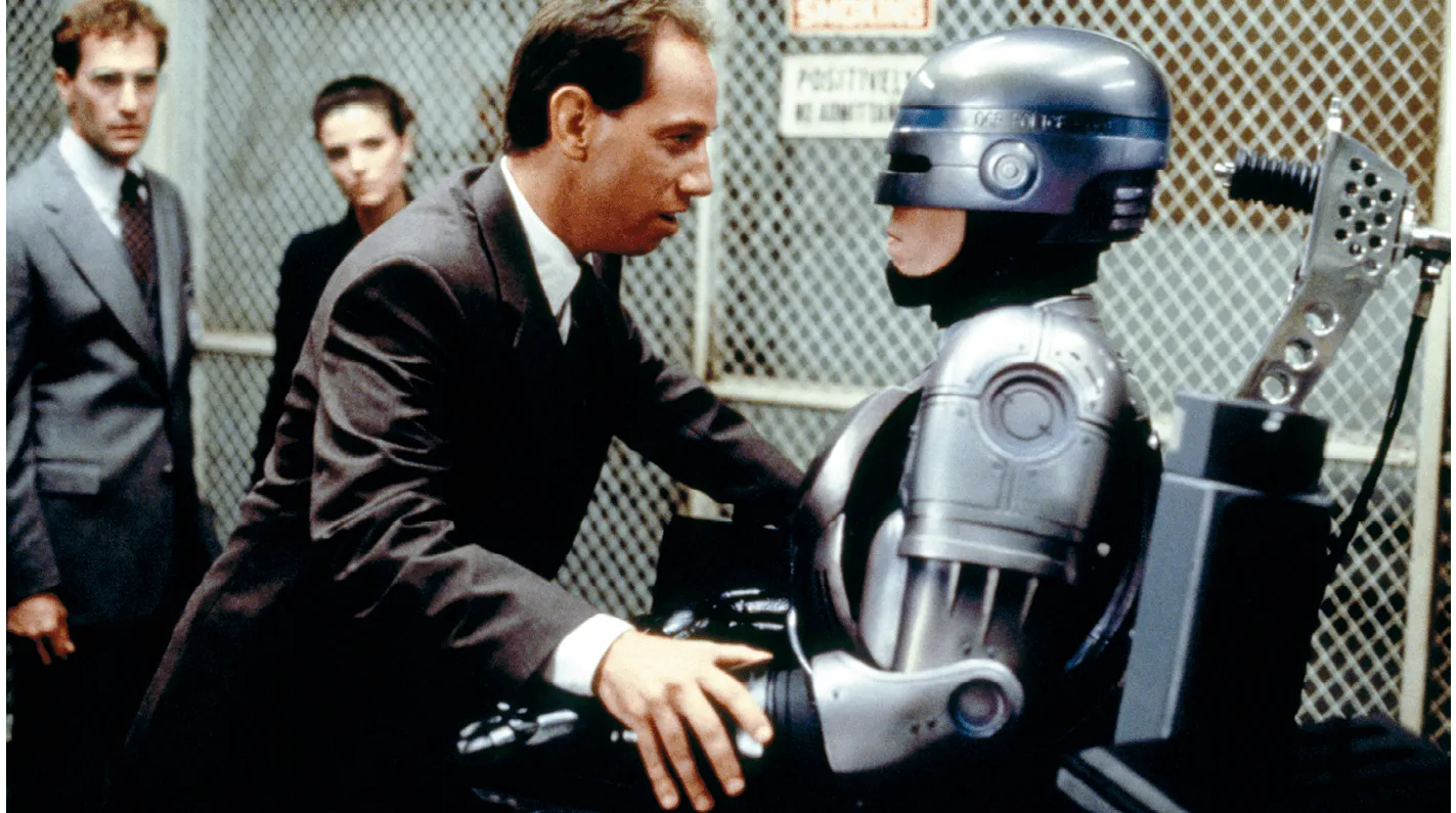 Photographie du film RoboCop : un homme en costume inspecte un RoboCop.