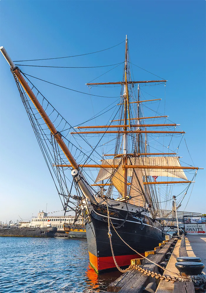 Photographie d'un grand voilier amarré à quai, ses voiles déployées.  Bateau historique, détails de cordages et mâts visibles.