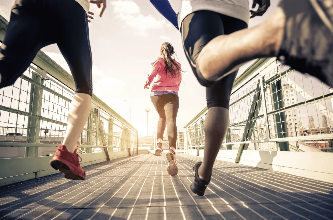 Photographie de trois coureurs vus de derrière, courant sur un pont métallique ensoleillé.