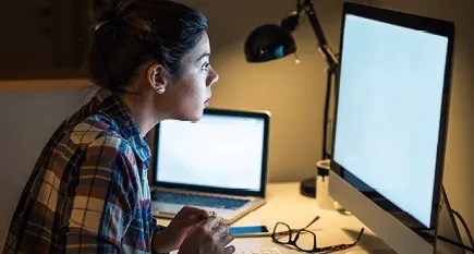 Photographie d'une femme concentrée travaillant tard sur son ordinateur, éclairée par une lampe de bureau.