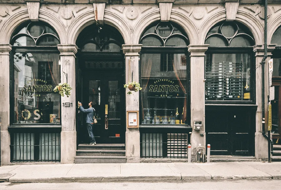 Photographie d'un restaurant Santos, un homme nettoie la devanture. Bâtiment en pierre, style classique, devanture noire avec vitrines.