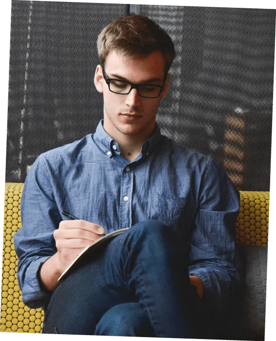 Photographie d'un jeune homme aux lunettes écrivant sur un carnet.