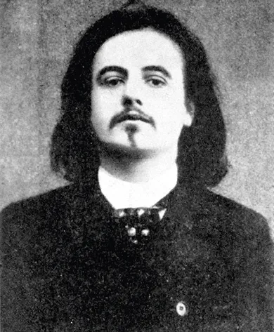 Photographie en noir et blanc d'Alfred Jarry, jeune homme aux longs cheveux foncés, vêtu d'une veste sombre et d'un nœud papillon.