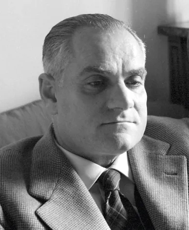 Photographie en noir et blanc d'Alberto Moravia, écrivain italien, assis, vêtu d'un costume et d'une cravate.