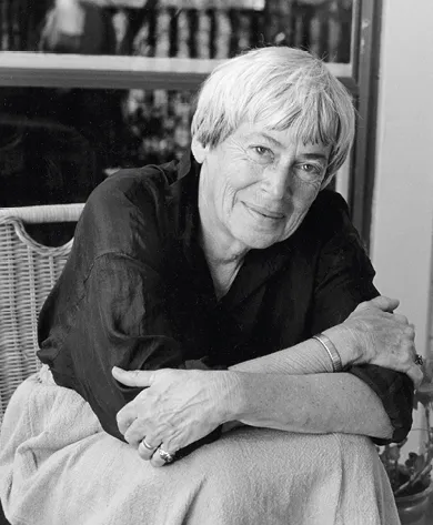 Photographie en noir et blanc d'Ursula K. Le Guin, écrivaine américaine, assise, les bras croisés.