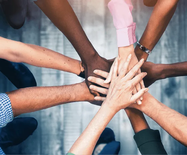 Photographie de mains entrelacées, symbolisant l'engagement et le travail d'équipe. Diversité des personnes représentées.