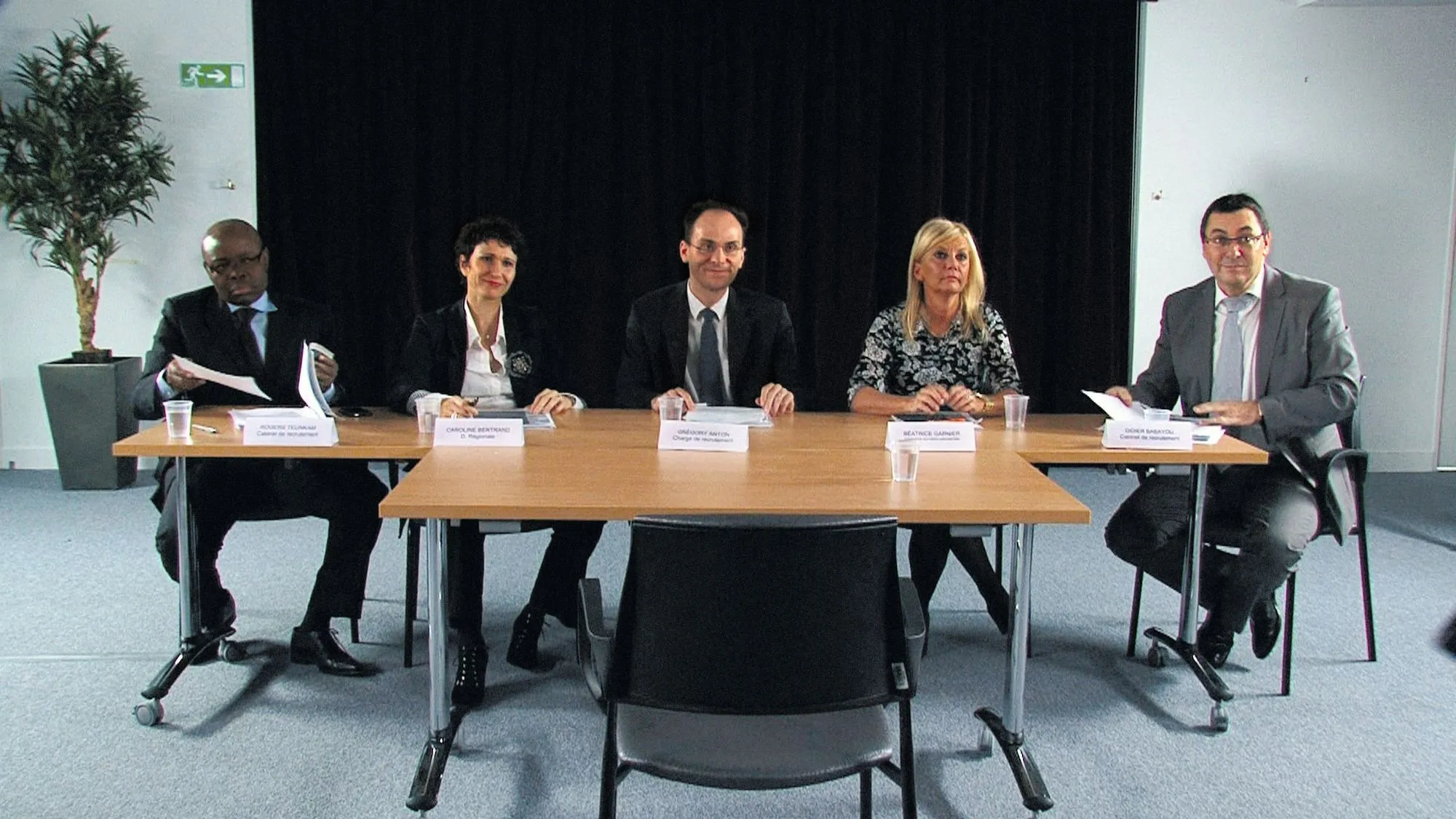 Photographie d'un jury d'entretien d'embauche composé de quatre personnes assises autour d'une table. Une chaise vide est face à elles.