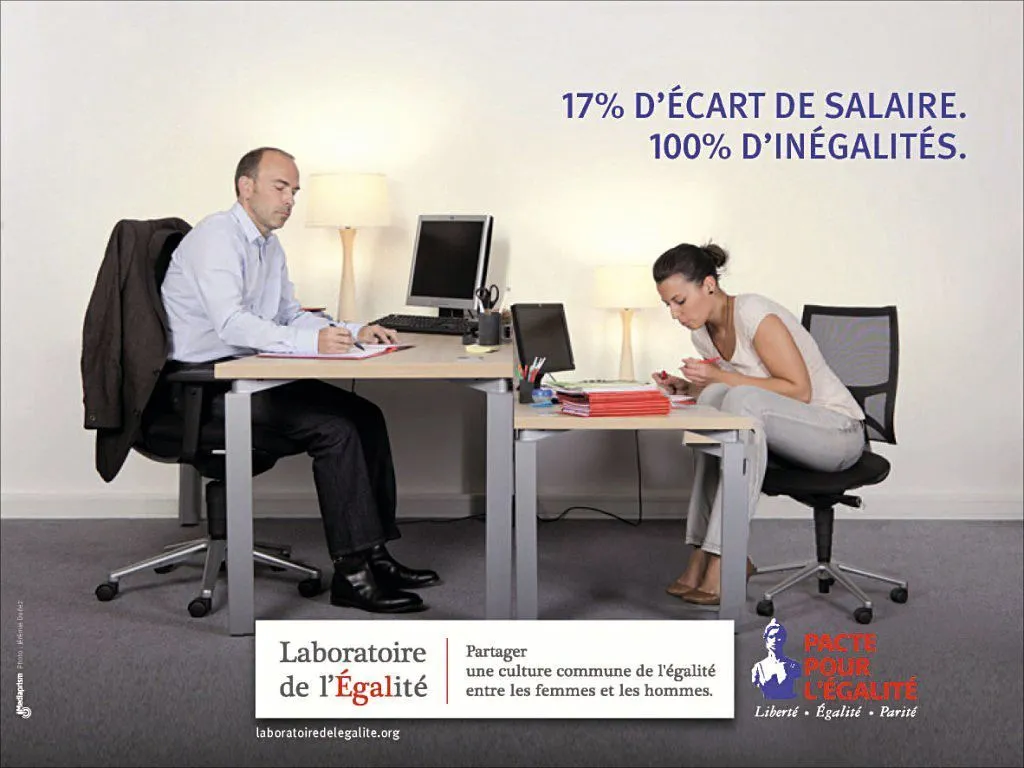 Photographie: homme et femme travaillent à des bureaux séparés. Ils semblent inégalement payés, illustrant les inégalités salariales entre les sexes.