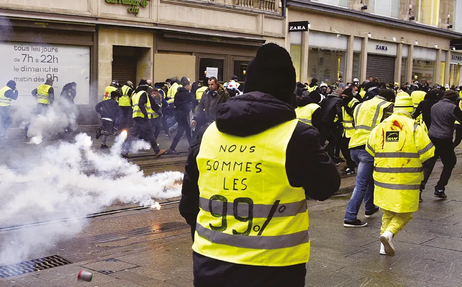 Photographie d'une manifestation des Gilets Jaunes, des manifestants portant des gilets jaunes et utilisant des fumigènes dans la rue.